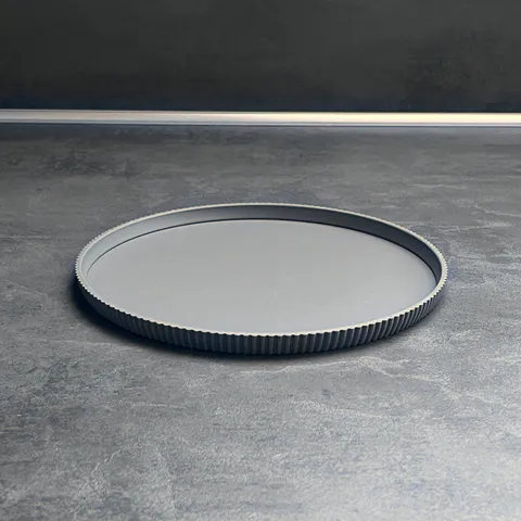 Dekoteller rund gerippt, Ø 21 cm von Slick: Dekoteller rund auf der Küchenplatte vor dunkler Wand, 3D-Druck aus mattem PLA in Grau