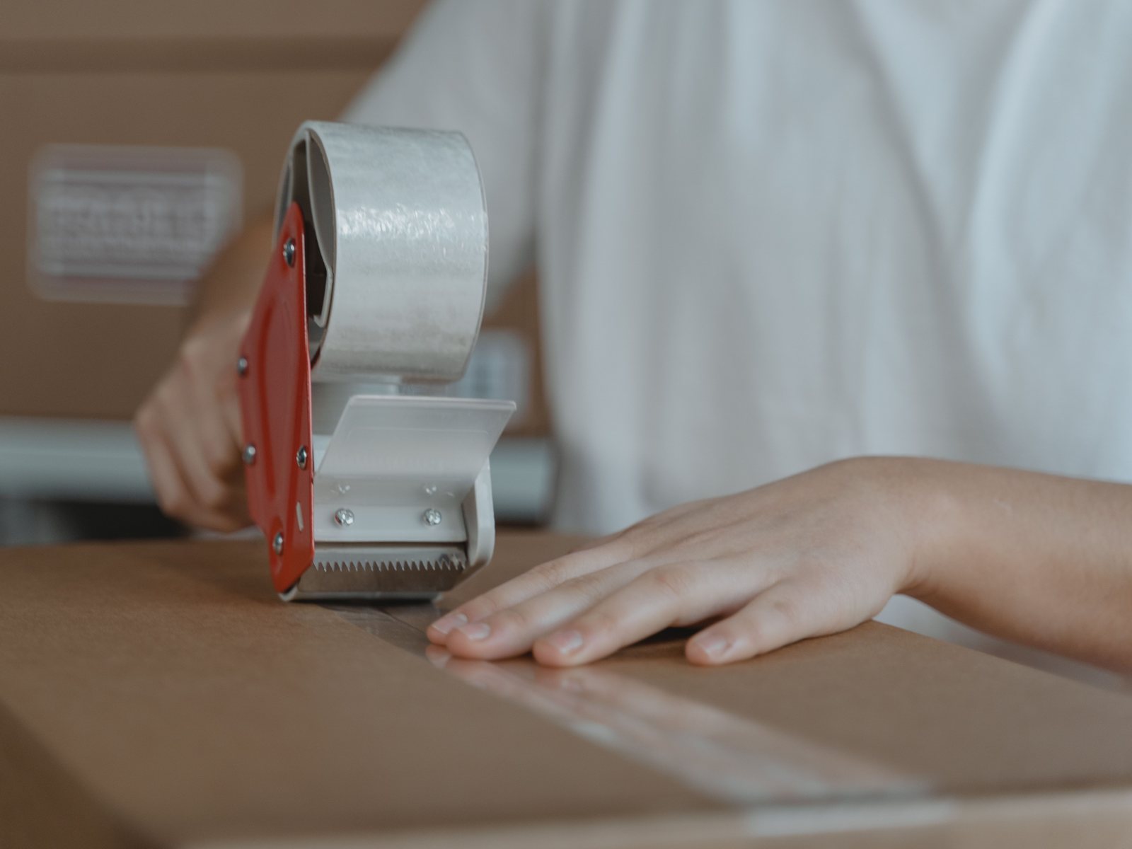 Tape dispenser sealing a shipping box at a packing table