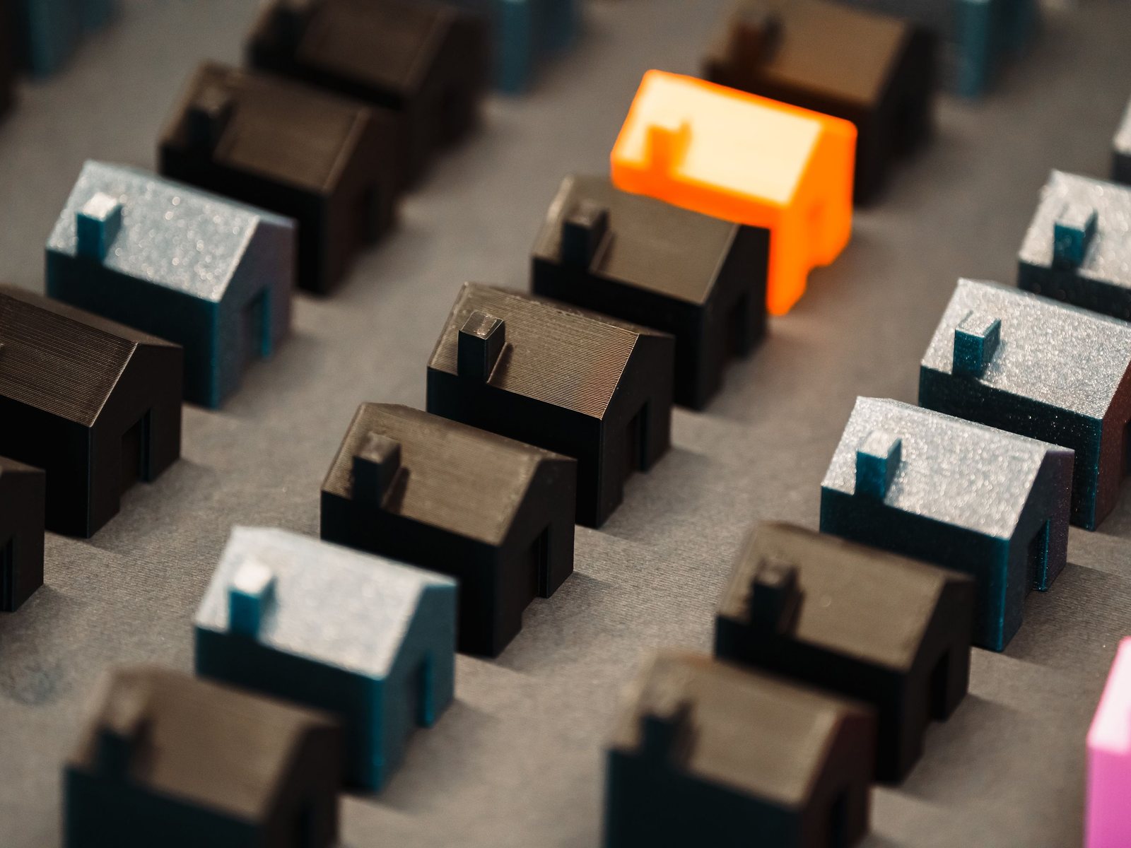 Rows of identical 3D-printed little houses in black, teal, orange and pink